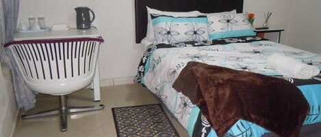 A bedroom with a bed, a chair, a coffee maker, and a small table with a vase.