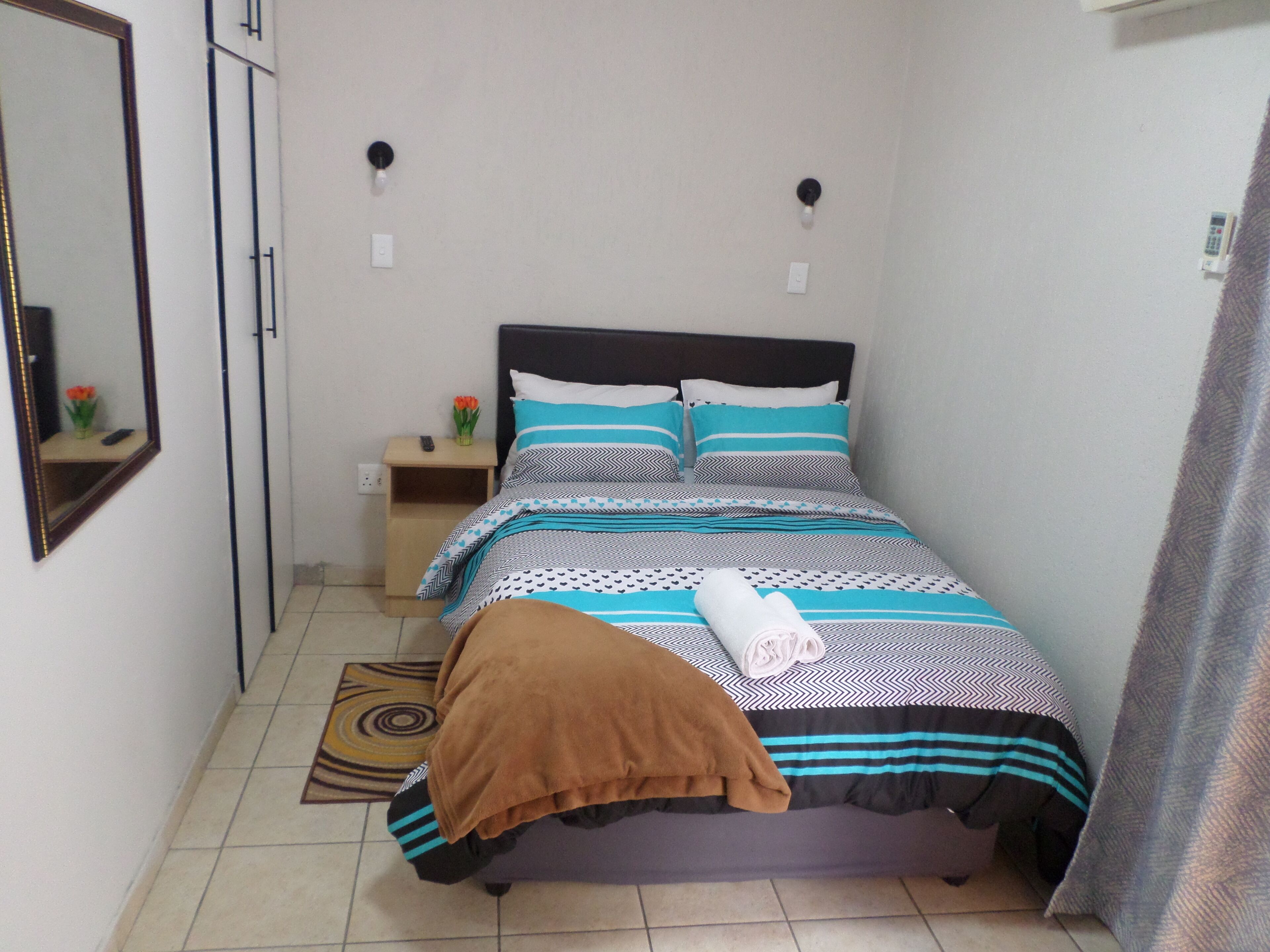 Un dormitorio ordenado con cama, mesitas de noche, un espejo y una lámpara de pared.