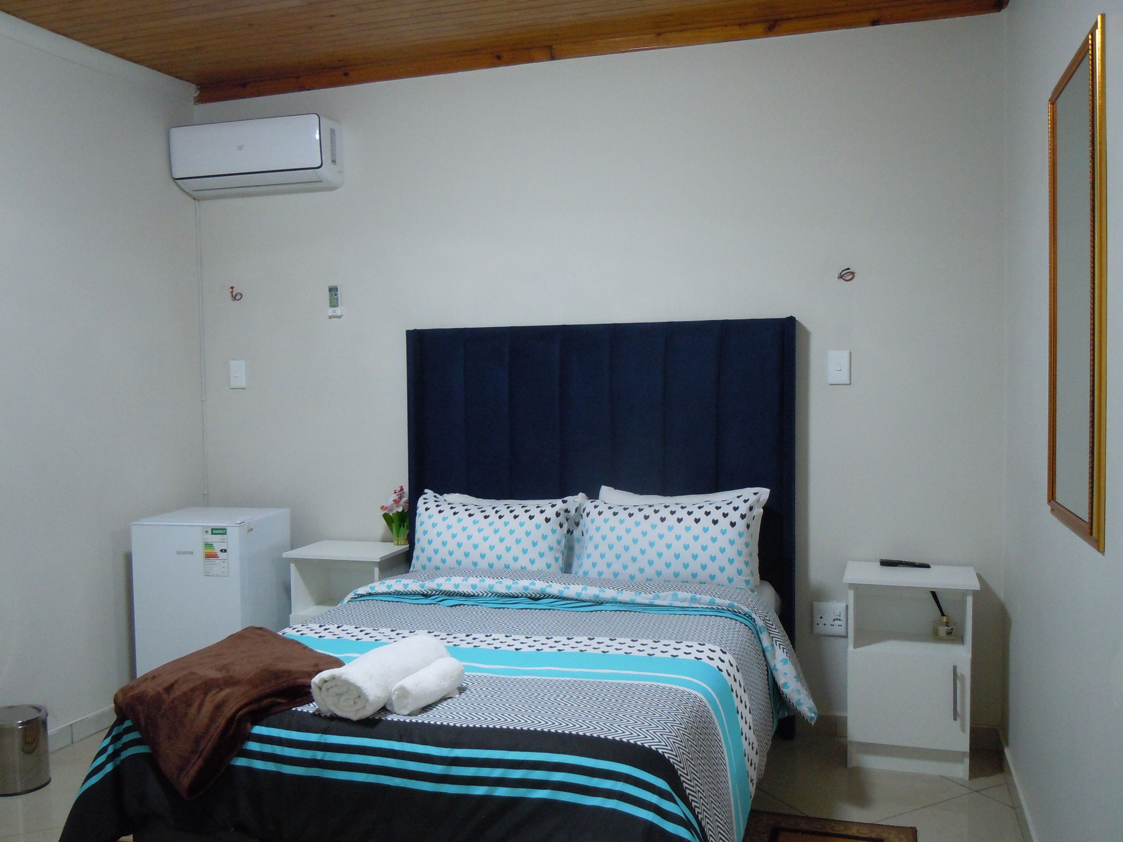 A bedroom with a bed, a small white cabinet, a heater, and a mirror.