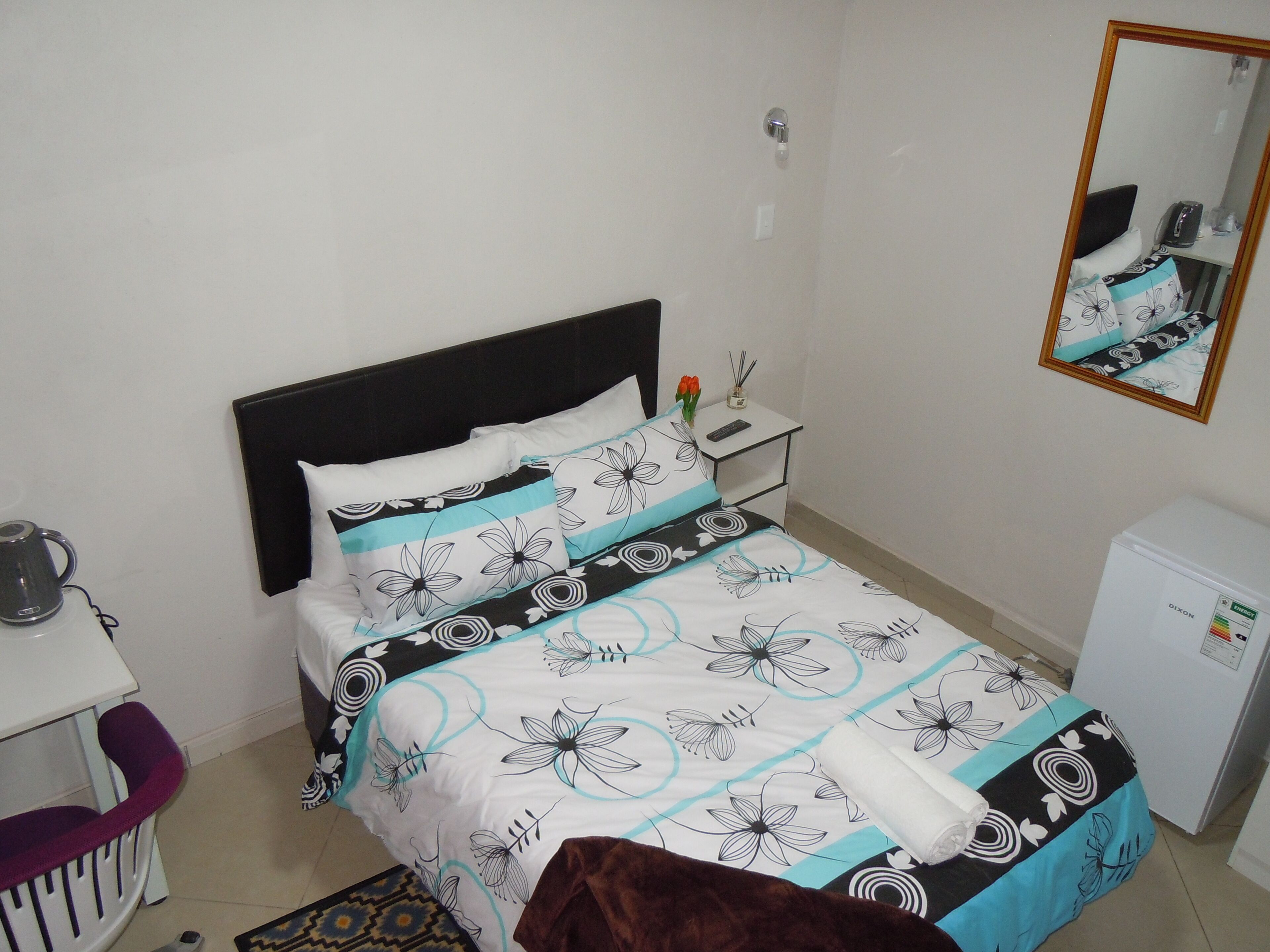 Une chambre bien rangée, avec un lit, une table de chevet et un petit réfrigérateur.