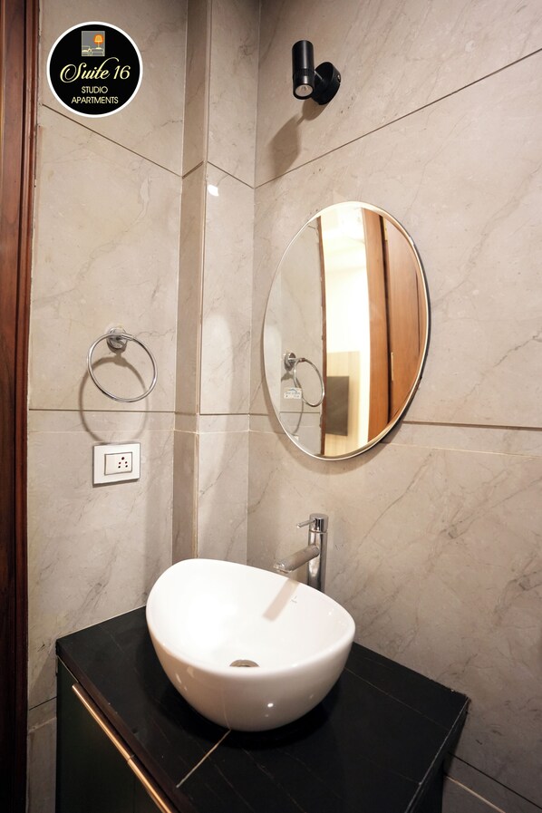 A bathroom with a white sink, a round mirror, and a towel ring. - Suite 16 Studio Apartment (Gurugram)