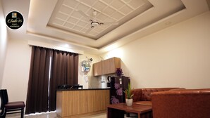 A modern living room with a sofa, a coffee table, and a kitchen area with wooden cabinets and a refrigerator. - Suite 16 Studio Apartment (Gurugram)