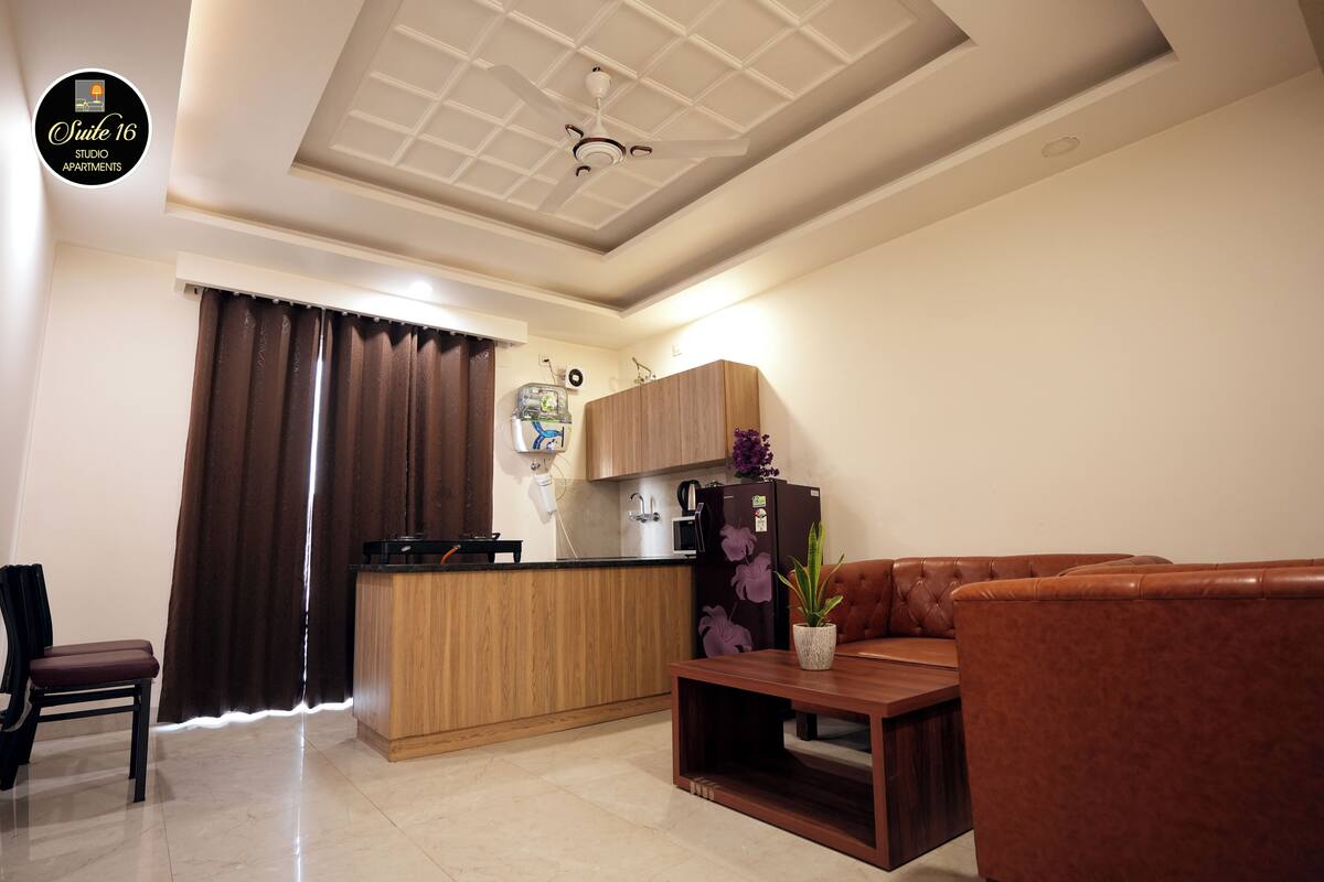 A modern living room with a sofa, a coffee table, and a kitchen area with wooden cabinets and a refrigerator.