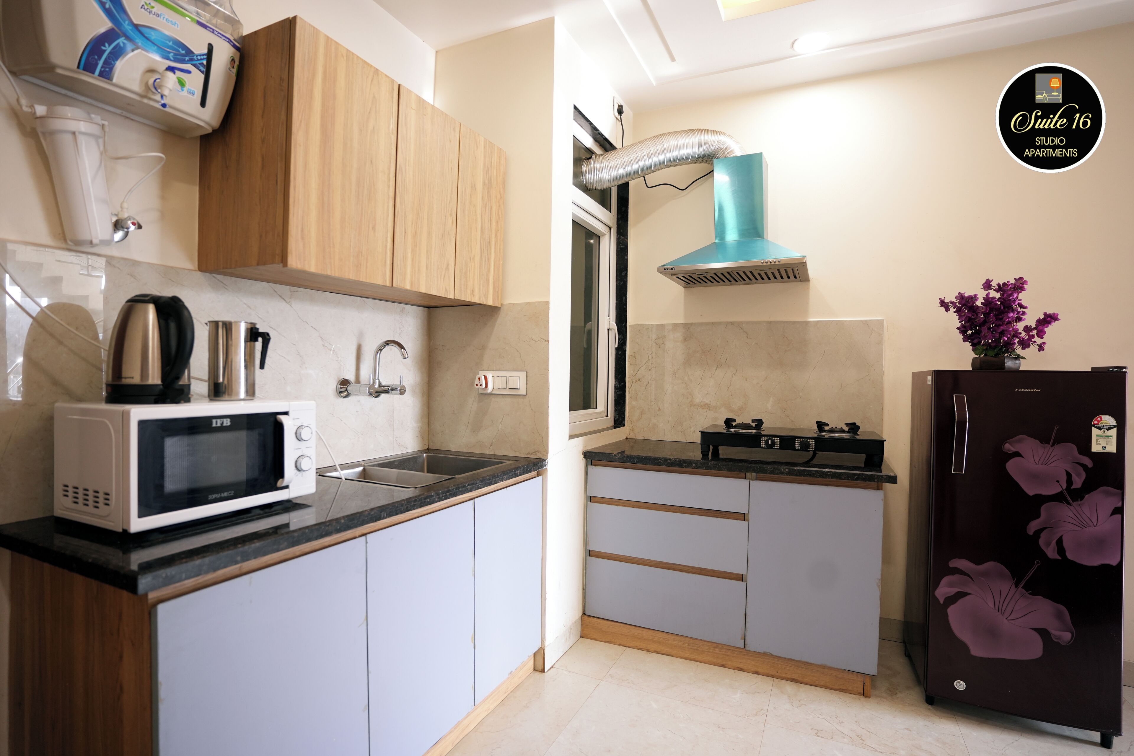 A modern kitchen with a microwave, kettle, sink, and a refrigerator with a floral design.