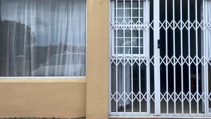 Un edificio con fachada color beige, un ventanal con cortinas blancas y una entrada con rejas.
