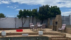 Una piscina con juguetes inflables, un patio de ladrillo con mobiliario exterior y una chimenea de piedra.