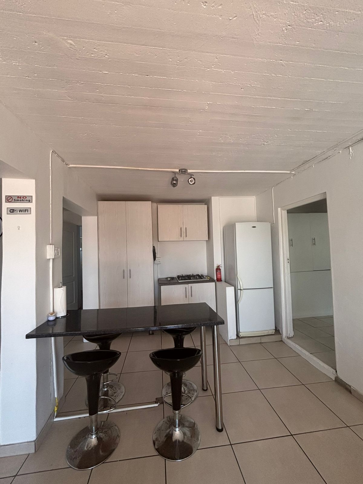 Une cuisine avec une table noire et deux tabourets de bar, un réfrigérateur blanc et une cuisinière à gaz.