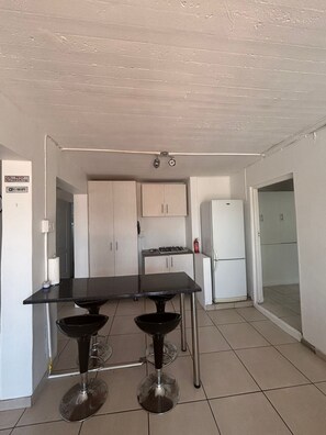 Eine Küche mit einem schwarzen Tisch, zwei Barhocker, einem weißen Kühlschrank und einem Gasherd.