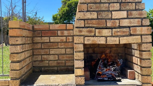 Un horno de ladrillo al aire libre con fuego encendido, rodeado por una cerca de metal.