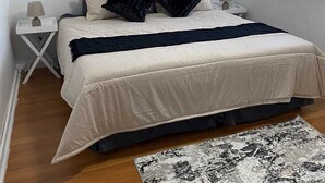 Un dormitorio con cama, mesitas de noche, una planta en maceta, una ventana con cortinas y una alfombra.
