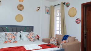 Un dormitorio con cama, sofá, ventana con cortinas y adornos en las paredes.