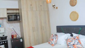 Un dormitorio con cama, armario, microondas, refrigerador y una pequeña cocina con estufa.