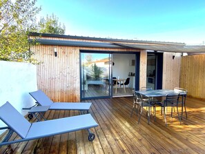 Een modern terras buiten, met een houten vloer, een glazen deur naar een binnenruimte en een tafel met stoelen.