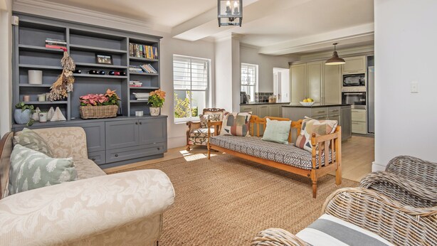 Un salón amplio con un sofá, un sillón de mimbre y una estantería llena de libros y objetos decorativos.