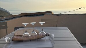 A table set with snacks, a sausage, and wine glasses on an outdoor terrace with a view of the landscape. - CAP Hélios, L'écrin Corse.  Breathtaking sea and pool views (Morsiglia)