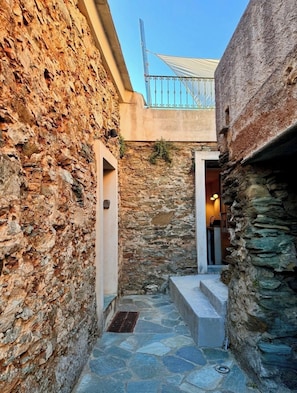 A narrow stone courtyard with a metal gate, stone walls, and a small entrance leading to a room. - CAP Hélios, L'écrin Corse.  Breathtaking sea and pool views (Morsiglia)