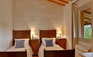 Une chambre à coucher avec deux lits en bois, chacun étant muni d’une table de chevet, d’une lampe et d’un oreiller à carreaux.