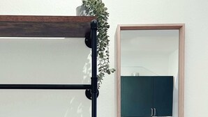 Habitació amb un mirall que reflecteix una zona de cuina, un suport metàl·lic negre i una planta en test.