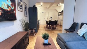 Un saló modern amb un sofà, una taula de centre i una televisió. Es pot veure una zona de menjador al fons amb una taula i cadires.