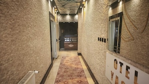 Un couloir avec une moquette à motifs, un radiateur et une enseigne indiquant « HÔTEL YASIN ».
