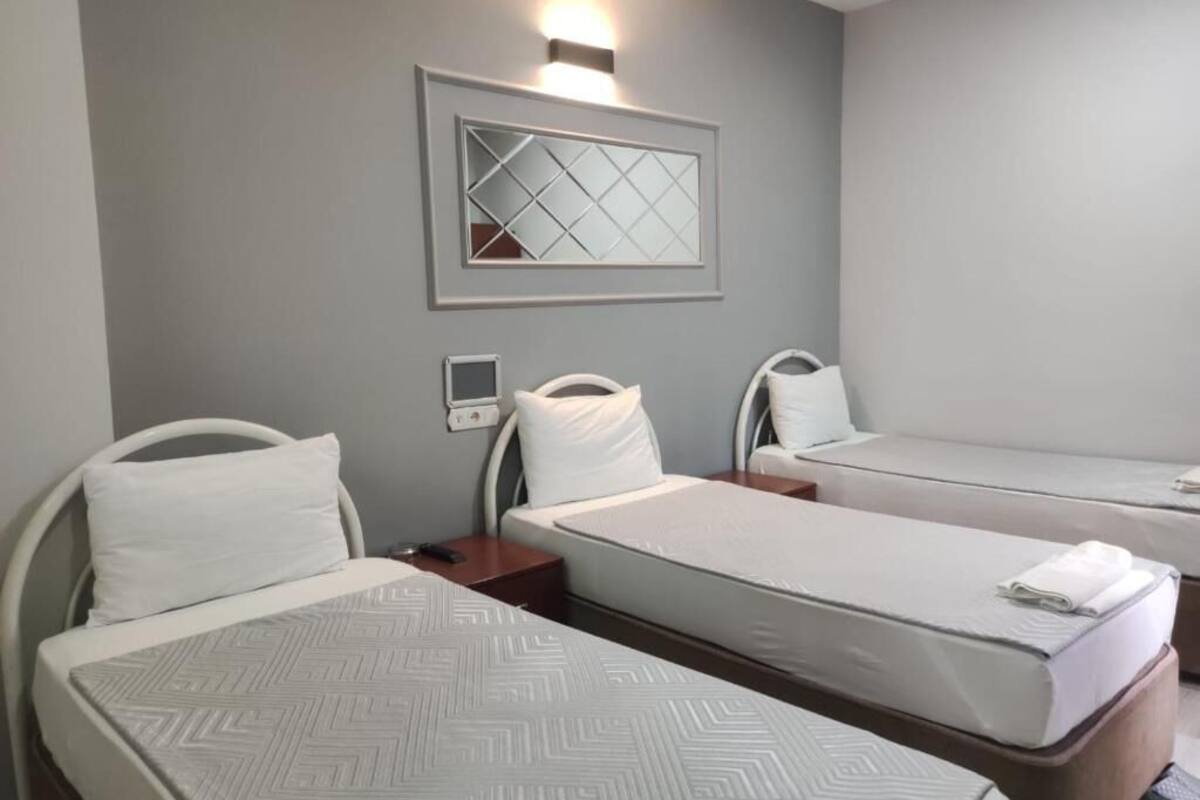 A hotel room with two single beds, a bedside table with a lamp, a wall-mounted TV, and a mirror.