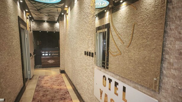 Un couloir avec un tapis, une enseigne indiquant « OTEL YASIN », et un espace de réception en arrière-plan.