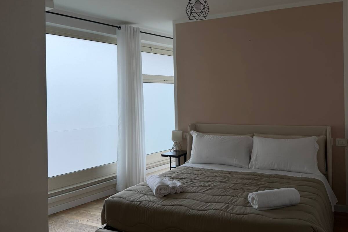 Une chambre avec un grand lit, une table de chevet avec une lampe et une vue par la fenêtre.