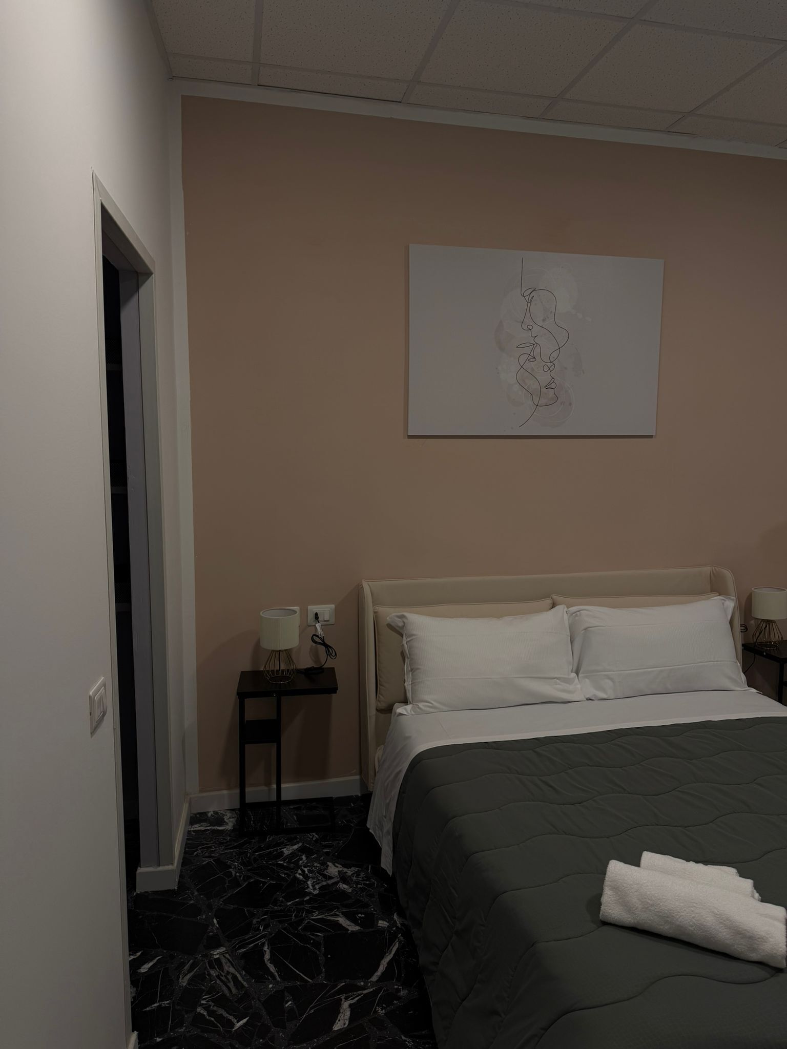 Una camera d'albergo con un letto, un comodino, un'opera d'arte a parete e una porta.