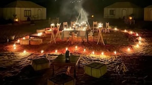 Ein kreisförmiges Arrangement aus Tischen und Stühlen mit Kerzen, umgeben von Zelten auf einem Campingplatz.