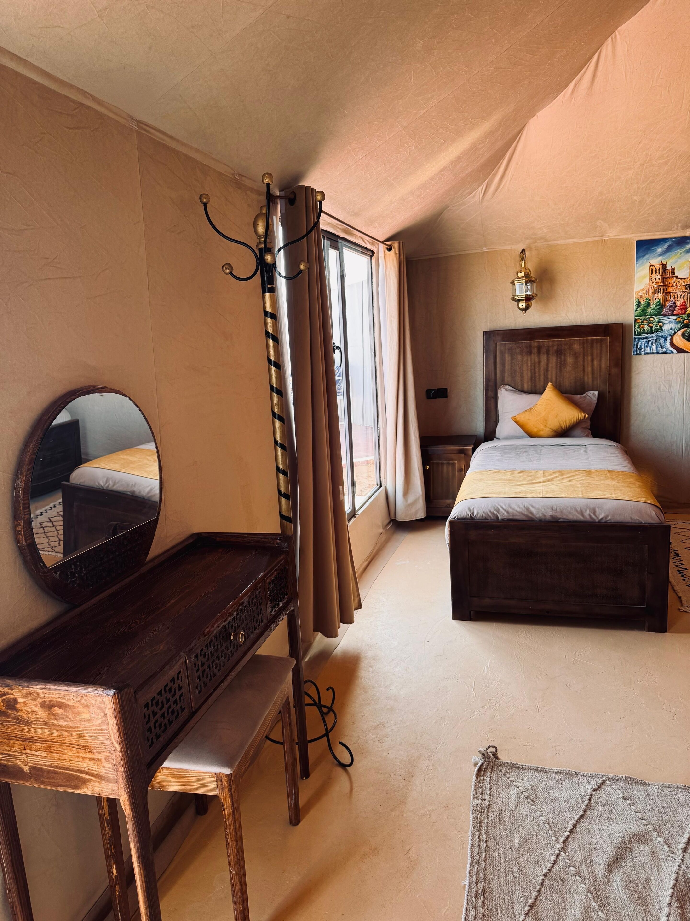 Une chambre à coucher comprenant un lit, une table de chevet, un miroir, des rideaux et une lampe fixée au mur.