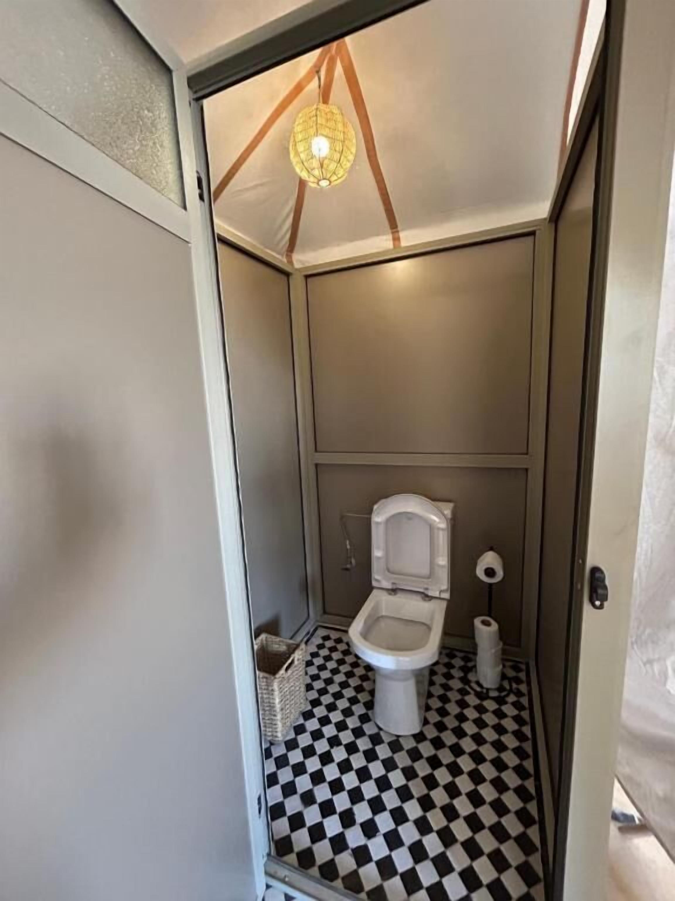 A compact, modern bathroom with a checkered floor, a toilet, and a hanging light fixture.
