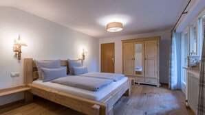Un dormitorio con cama de madera, dos mesitas de noche, un armario y una ventana con cortinas.