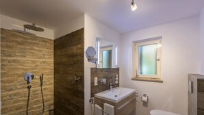 Un baño moderno con pared de madera, cabina de ducha de cristal, lavabo con espejo y retrete.