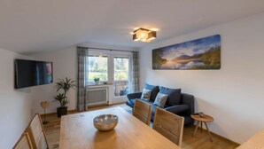 Una sala de estar moderna con una mesa de comedor de madera, un sofá azul, un cuadro y un televisor montado en la pared.