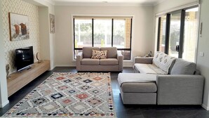 A modern living room with a large window, a grey sofa, a TV on a wooden stand, and a patterned rug. - Modern Seaside Boho Incl Breakfast (Cowes)