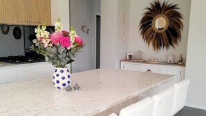 A modern kitchen with a marble countertop, white bar stools, and a vase of flowers. - Modern Seaside Boho Incl Breakfast (Cowes)