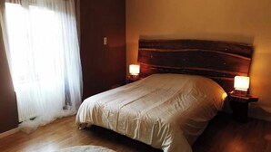 A bedroom with a wooden headboard, a large bed, two bedside lamps, and a window with sheer curtains. - Character house in the heart of the baume les messieurs valley (Baume-les-Messieurs)