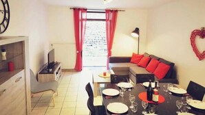 A dining area with a table set for four, a sofa with red cushions, a clock on the wall, and a window with red curtains. - Character house in the heart of the baume les messieurs valley (Baume-les-Messieurs)