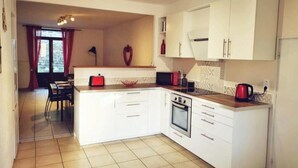 A modern kitchen with white cabinets, a microwave, a kettle, and a dining area with a table and chairs. - Character house in the heart of the baume les messieurs valley (Baume-les-Messieurs)