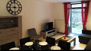 A dining area with a table set for four, a television on a stand, and a window with red curtains. - Character house in the heart of the baume les messieurs valley (Baume-les-Messieurs)