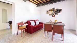 A living area with a red sofa, a wooden dining table, and a modern abstract art piece on the wall.