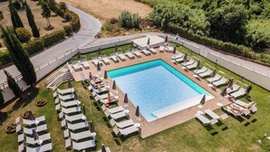 An aerial view of a resort with a central swimming pool surrounded by sun loungers and a grassy deck.