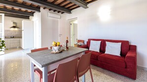 A modern kitchen with white cabinets, a dining table with chairs, and a red sofa in a living area.
