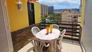 A balcony with a table and chairs, a stone wall, and a view of buildings in the background. - Nicpa atico Los Cristianos (Los Cristianos)