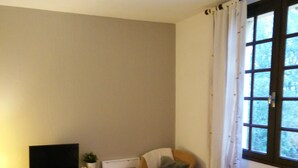 Una sala de estar con un sofá, una mesa baja con velas, un televisor en un estante y un ventanal con cortinas.