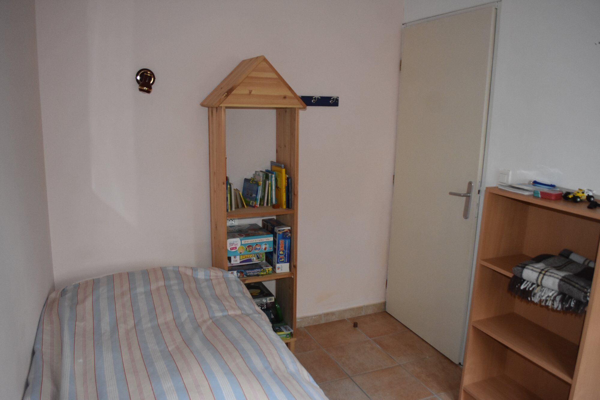 Ein Schlafzimmer mit einem Bett, einem Holzregal mit Büchern, einem Kleiderschrank und einer Tür.
