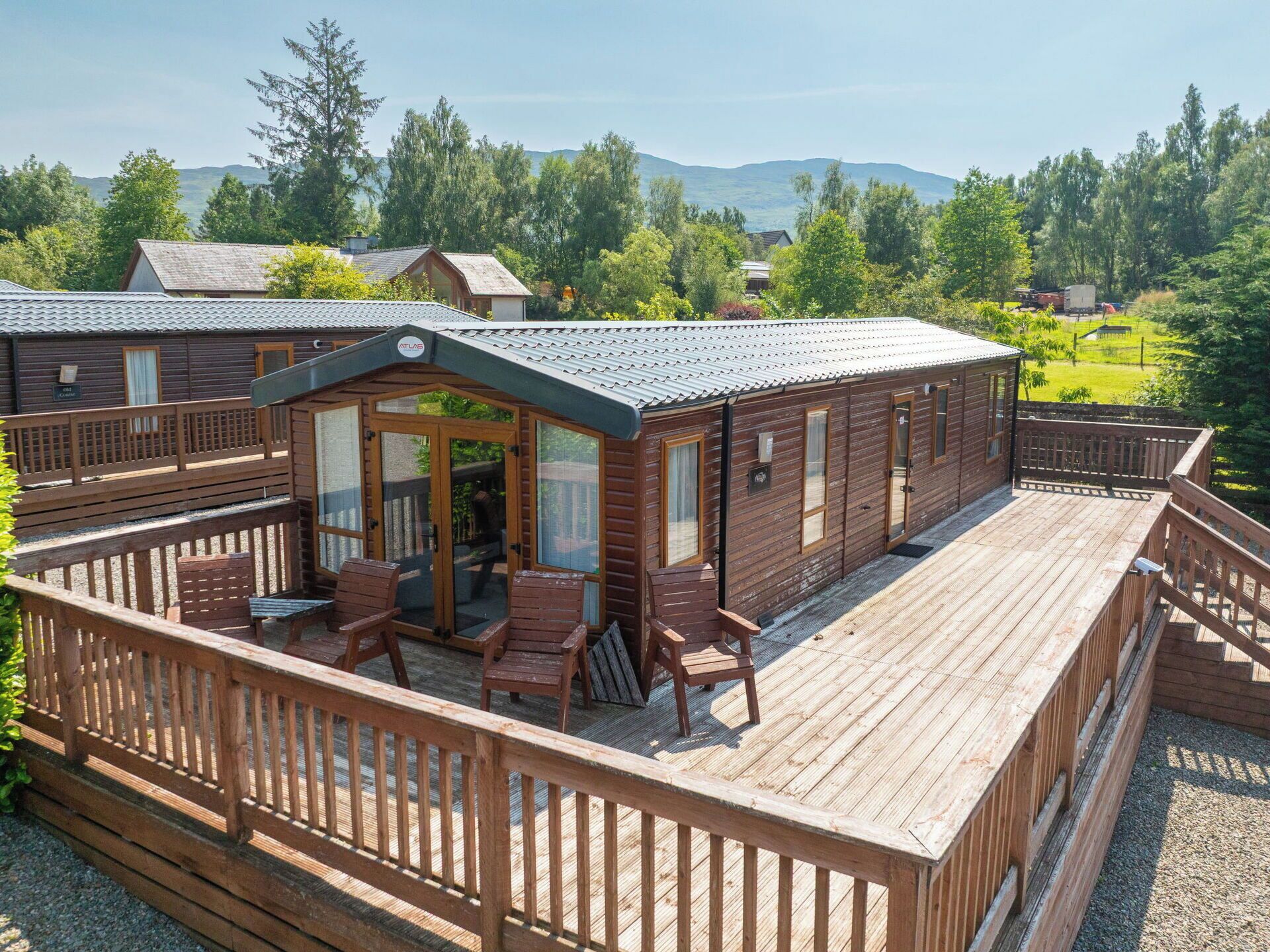 A wooden cabin with a deck, outdoor seating, and a view of the surrounding forest and hills.