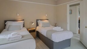 Ein Hotelzimmer mit zwei Einzelbetten, einem Nachttisch mit Lampe und einer Tür zu einem anderen Raum.