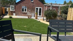 Ein Garten mit einem Ziegelhaus, einer Holzterrasse und einem Rasen.