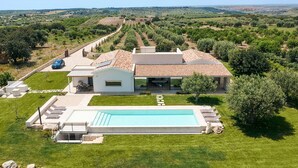 Una casa moderna con piscina, rodeada de vegetación exuberante y olivares.